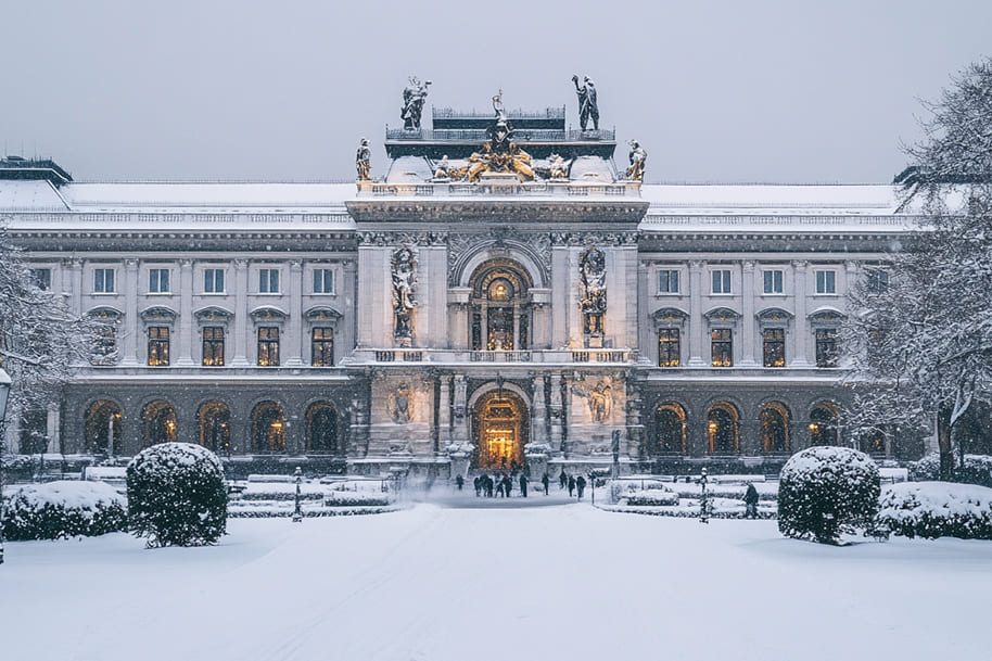 A breathtaking winter view of a grand historic building in Vienna, adorned with statues and illuminated lights, surrounded by a snowy garden. The perfect blend of architectural elegance and seasonal charm, making it one of the top winter travel destinations!